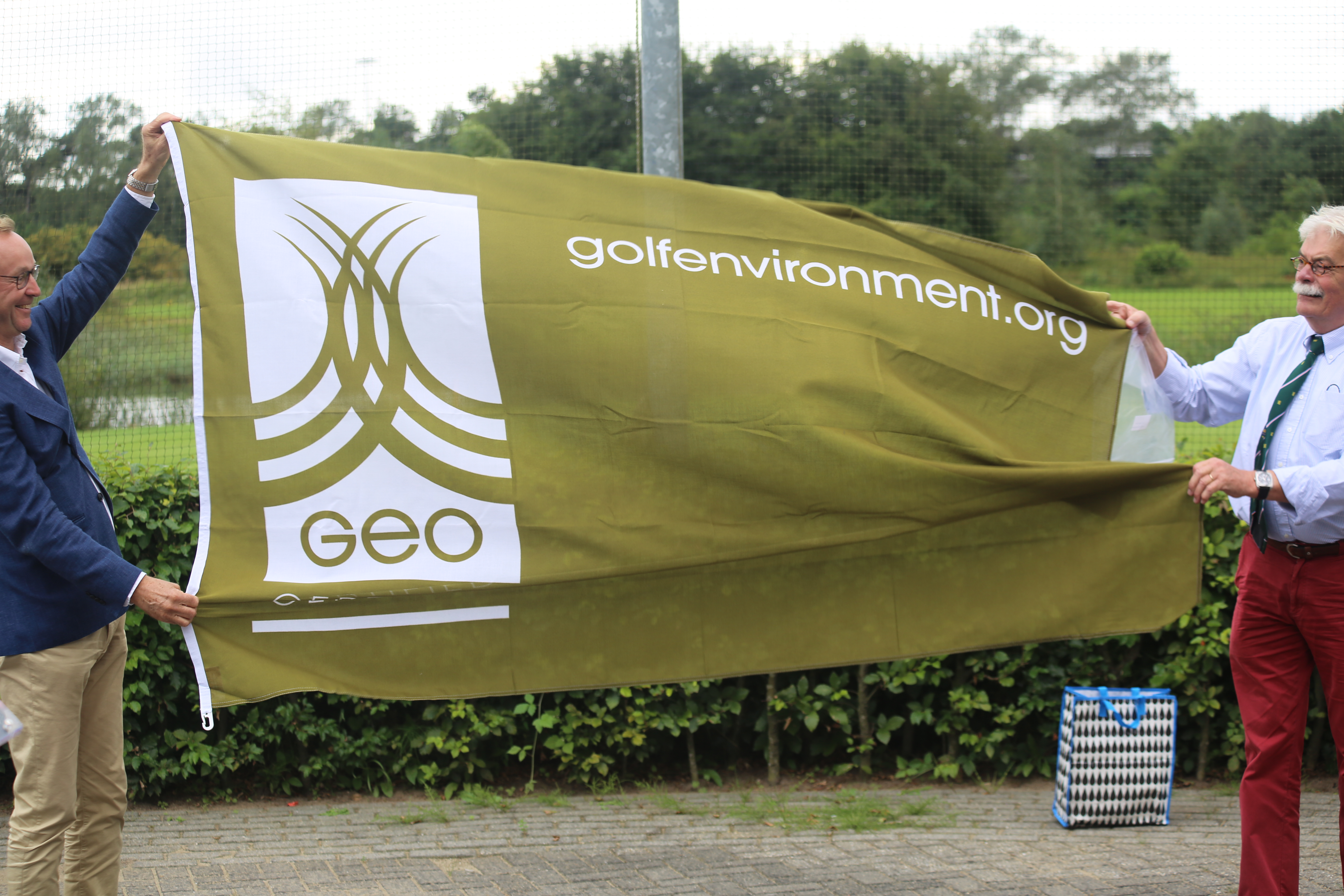 Voorzitter van Golfpark Spandersbosch Tom Kuc (links) en de heer Van Keulen (NGF) ontvouwen de GEO-vlag