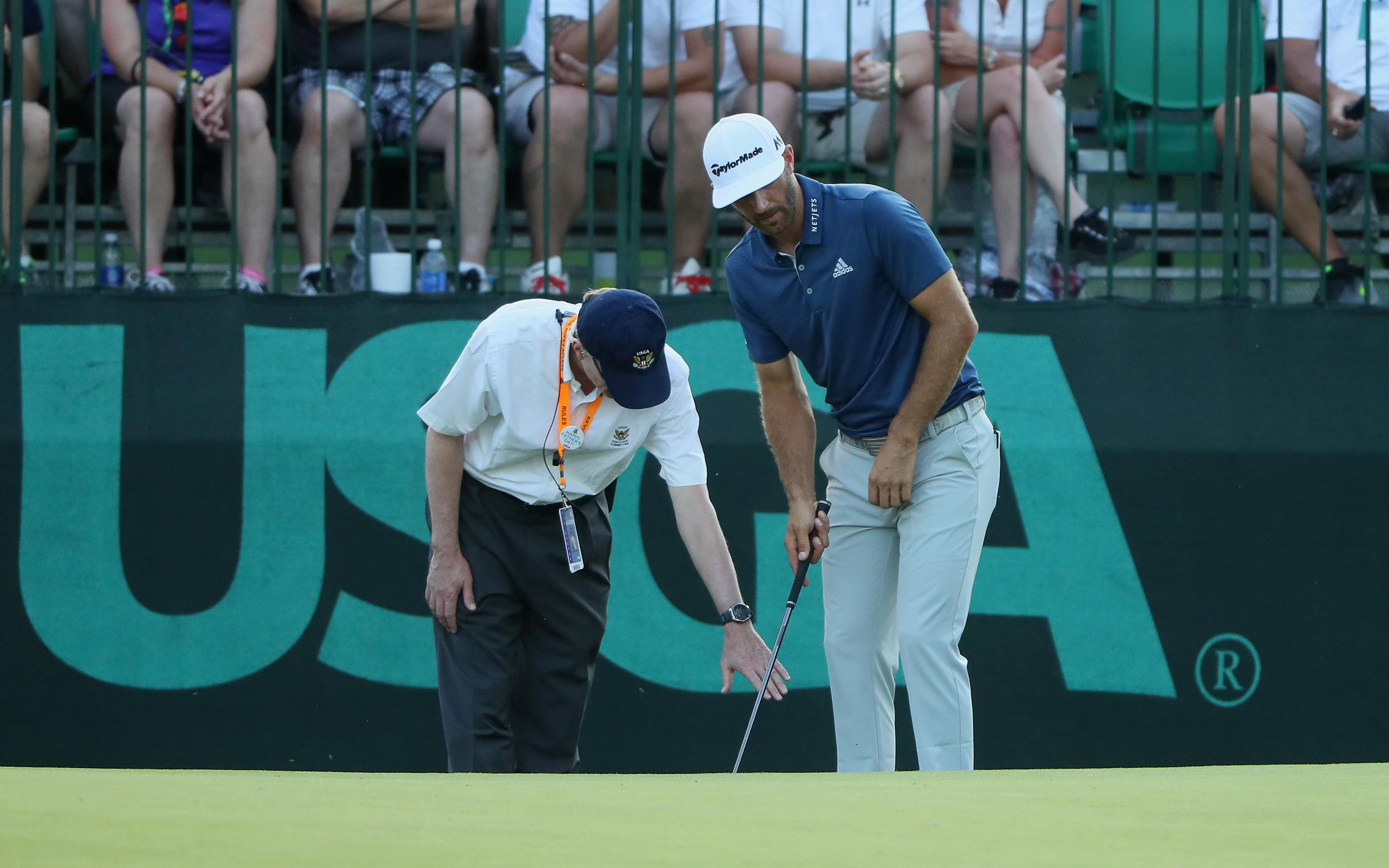 Dustin Johnson en een referee in het US Open nadat de bal op de green verrold was.